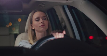 Tired young caucasian woman is driving a car on a road looking around. Road from work. Car's interior. Front view. Close up.