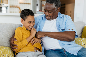 Happy grandfather tickling his grandson while sitting at home. Bonding and unconditional love concept. - 446445611