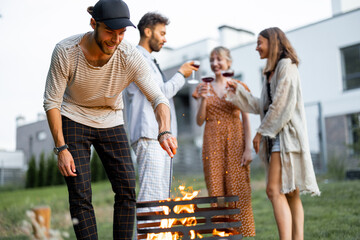 Friends have a picnic, making fire at barbeque, talking and drinking wine on the green lawn at...