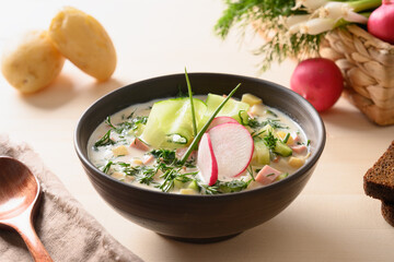Homemade summer Okroshka soup with kefir and summer vegetables on light wooden table. Close up.