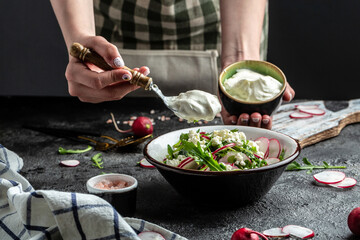 cooking spring salad with red radish, arugula and cottage cheese dressed with sour cream