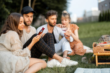 Young friends sit together and hug, talk and drink alcohol in a close and friendly atmosphere on a picnic in the evening