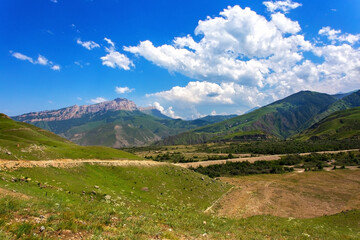 Mountain landscape view. Summer sunny day in valley. Panorama with hills, yellow sand, green grass and background of blue sky with white clouds.