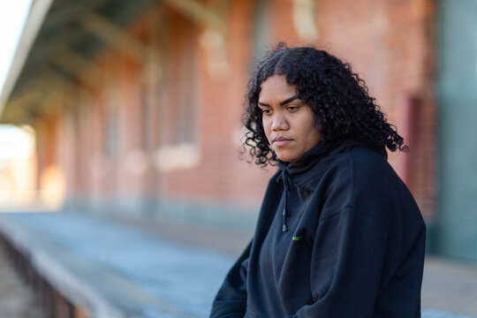 Young aboriginal woman wearing black hoody against blurred background of old station platform