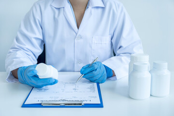 Doctor or nurse hand holding medicine pill bottle and write a prescription at the pharmacy office, healthcare, and medical check-up concept