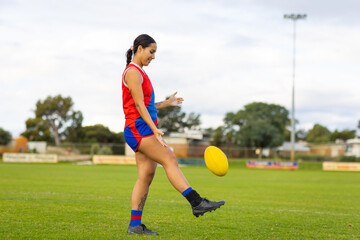 female Australian rules football player kicking ball