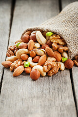 A mixture of fresh nuts spilled from a linen bag onto a gray wooden table.