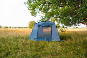 a tourist tent in nature under a tree. Summer vacation hiking