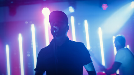Rock Band Performing at a Concert in a Night Club. Portrait of a Lead Singer Singing into Microphone. Live Music Party in Front of Bright Colorful Strobing Lights on Stage. 