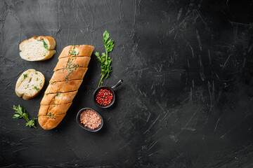 Garlic bread filled compound herb butter, on black dark stone table background, top view flat lay,...