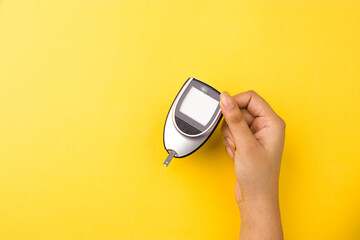 Blood glucose meter, the blood sugar value is measured on a finger on yellow background.