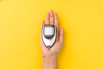 Blood glucose meter, the blood sugar value is measured on a finger on yellow background.