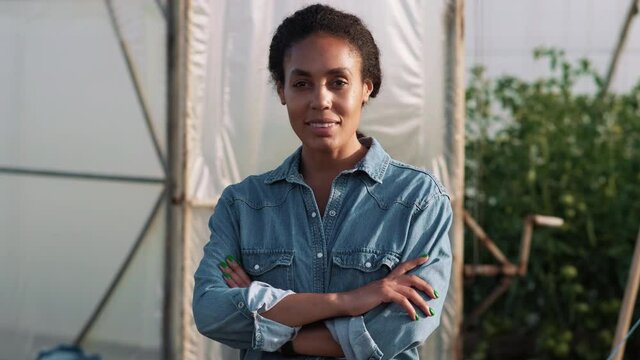 A beautiful afro-american woman is holding hands while looking to the camera standing at the greenhouse
