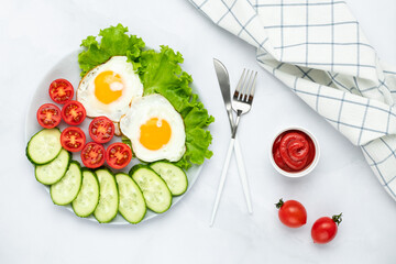 Fried chicken eggs with vegetables on a gray table. Breakfast concept. Top view. Flat lay composition. Food background in morning. Fresh sliced cucumbers and tomatoes.