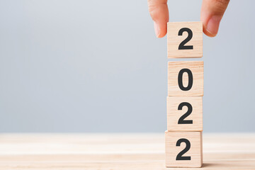 hand holding wooden cube block with 2022 text on table background. Resolution, plan, review, goal,...