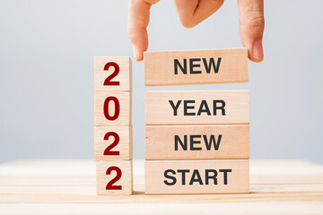 Businessman hand holding wooden block with text 2022 NEW YEAR NEW START on table background. Resolution, strategy, solution, business and  holiday concepts