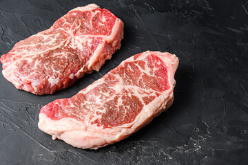 Organic top blade steak cuts, on black textured background side view with space for text.