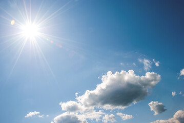 Naklejka na ściany i meble Heap, white clouds, sun with long rays and glare in the blue sky. Sky landscape