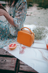 picnic by the lake, a white blanket, a woman's purse, fruit and a croissant