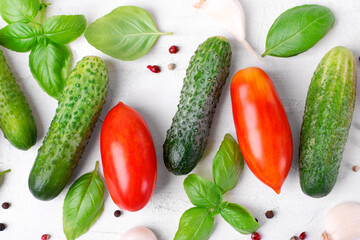 Cucumbers, plum tomatoes, basil leaves, garlic and pepper on the white table. Flat lay. Ingredients for a salad. Homegrown produce