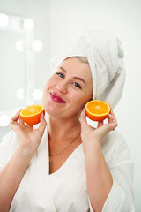 Fresh energy. Happy, joyful pretty woman smiling with white teeth, holding two halves of an orange and smiling, uses it for beauty treatments in the bathroom