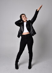 Full length portrait of young woman with natural brown hair,  wearing black leather scifi outfit with jacket, standing pose on light studio background.