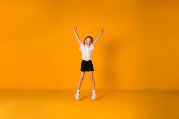 Fototapeta na wymiar a little blonde girl in a school uniform jumps on a yellow background with a place for text