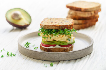Delicious healthy sandwich of gluten-free bread with flax and sunflower seeds with cream cheese (ricotta), egg salad, radish, avocado and microgreens. Breakfast. Diet. Healthy food