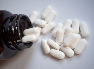 White medicinal pills are scattered from a brown bottle container close-up