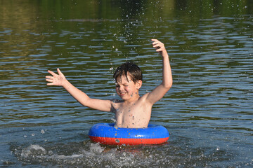 Child in water with inflate ring play and swim alone. Boy splashing in a water on hot sunny day