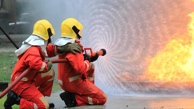Fireman in fire protection suit fighting strong fire in danger situation. Firefighters, Firemen spraying high pressure water or suitable extinguishing agents to fire .