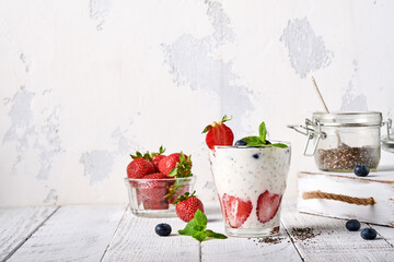 Two strawberry chia seeds layered smoothie or milkshake with strawberry and blueberry mint in glass on light grey background. Summer and healthy dieting drinks, vegetarian food concept.