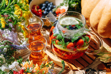 natural aromatic fruit tea in a transparent teapot and in a cup among berries and flowers. warming aromatic tea with a deep aroma of berries and wildflowers.