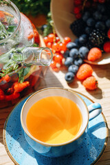 natural aromatic fruit tea in a transparent teapot and in a cup among berries and flowers. warming aromatic tea with a deep aroma of berries and wildflowers.