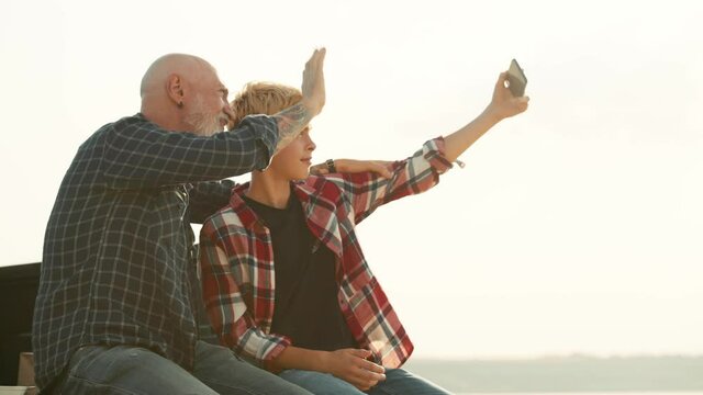 A positive son and his father are taking selfie photos on the pickup truck while travelling on nature