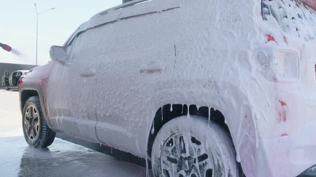 The car is covered with foam. The car is washed with soap at a car wash. Car wash with high pressure detergent
