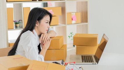 Fototapeta na wymiar Start a business smeA beautiful Asian businesswoman works with boxes and laptops to take orders from customers and enjoys working from home online selling ideas and delivery.