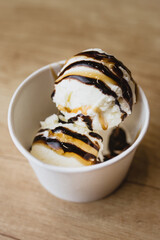 Balls of creamy ice cream with caramel and chocolate in a paper cup - top view