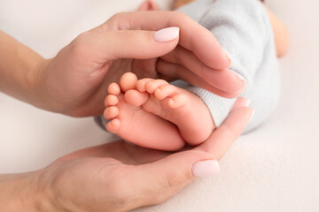 Female hands of young mother holding her newborn baby feet, closeup image with blur baby in background