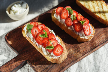Two toasts or bruschetta with strawberry and cream cheese on wooden board. Summer breakfast. Hard lighting - 446467066