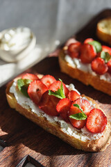 Two toasts or bruschetta with strawberry and cream cheese on wooden board. Summer breakfast. Hard lighting - 446467083