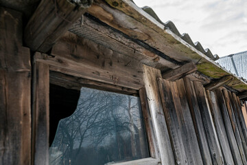 Fototapeta na wymiar Broken window by an old wooden utility shed. Reflection of trees in the window.