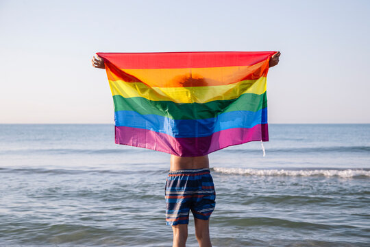 Young latino man raising a lgtbi flag on the beach