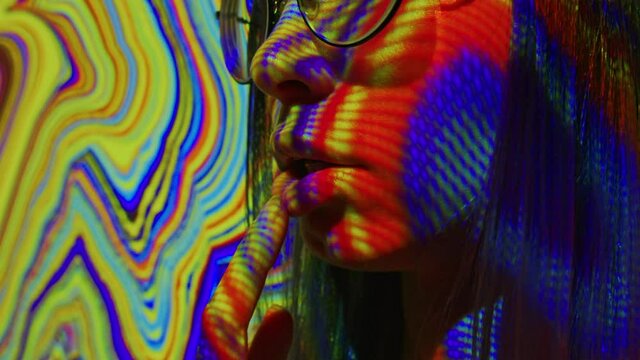 A young woman puts a lsd acid blotter on her tongue. Multicolored psychedelic abstract background. The concept of psychedelia, nirvana and addiction