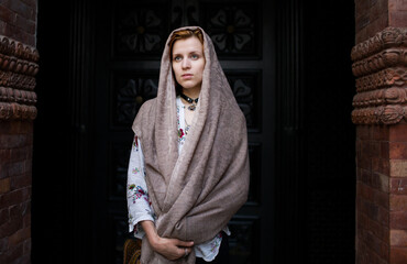 red hair woman in a cashmere scarf stands against the background of the door