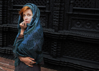red hair woman in a cashmere scarf stands against the background of the window