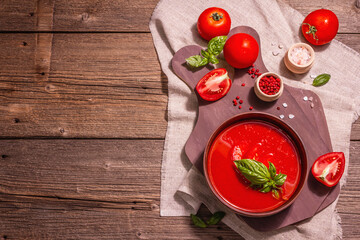 Tomato soup with basil in a bowl. Ripe vegetables, fresh greens, fragrant spices. Vintage wooden table, top view