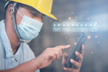 An engineer wearing a mask uses a smartphone to respond to satisfaction with building construction...