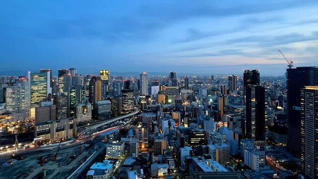 UMEDA, OSAKA, JAPAN : Aerial high angle sunset view of CITYSCAPE of OSAKA. View of buildings and street around Osaka and Umeda station. Wide view time lapse tracking shot, dusk to night.