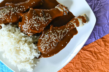 Close-up of chicken dish with mole sauce and rice on colorful background